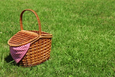 Photo of Wicker basket on green lawn prepared for picnic in park