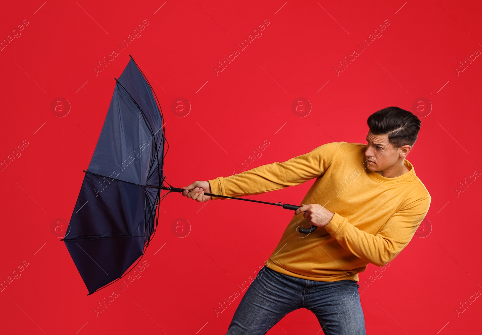 Photo of Emotional man with umbrella caught in gust of wind on red background