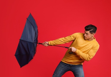 Photo of Emotional man with umbrella caught in gust of wind on red background