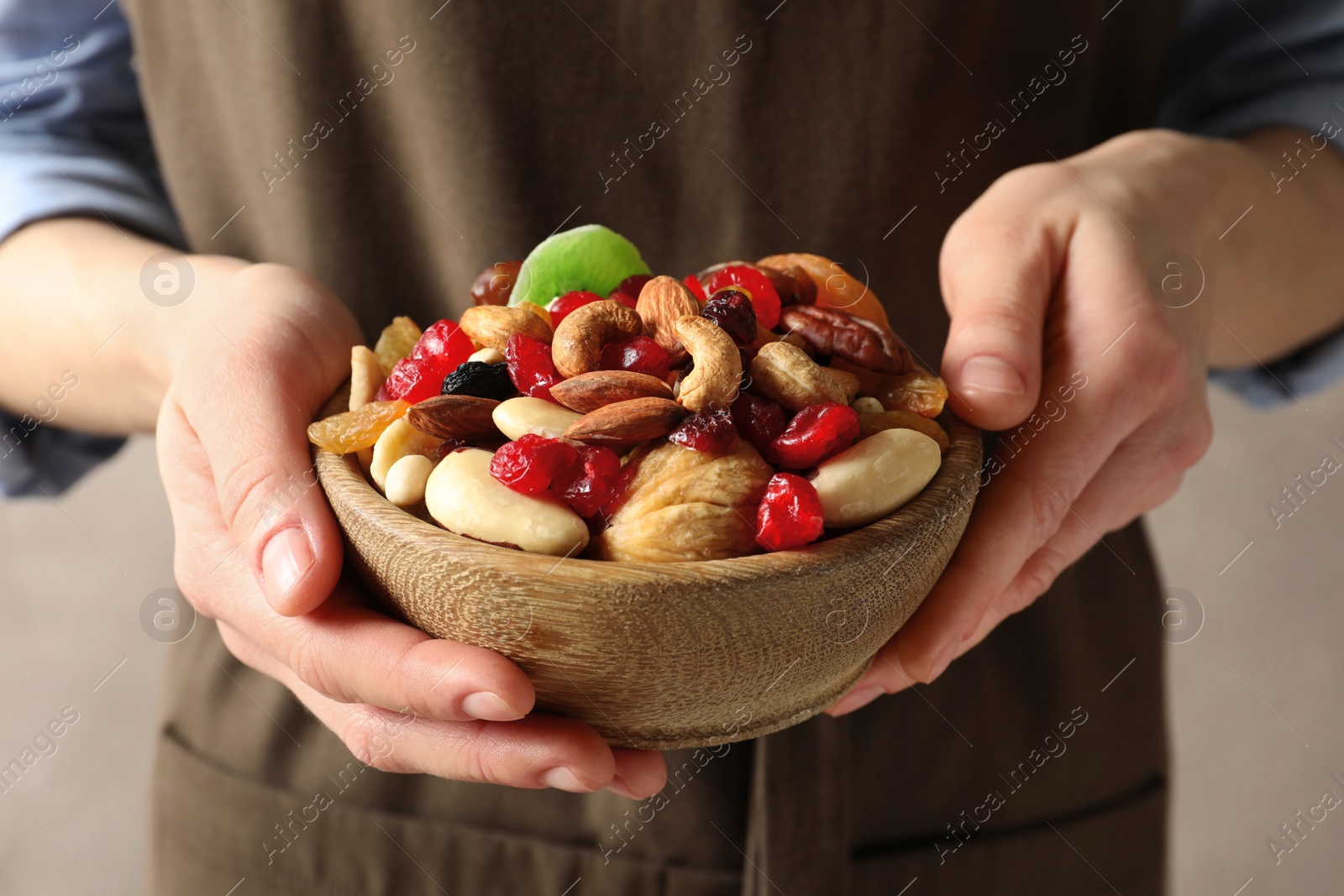 Photo of Young woman holding bowl with different dried fruits and nuts, closeup