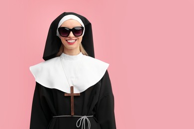 Photo of Woman in nun habit and sunglasses against pink background. Space for text