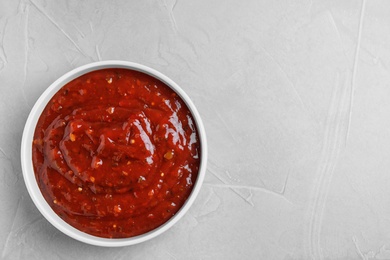 Photo of Bowl of hot chili sauce on light background, top view. Space for text