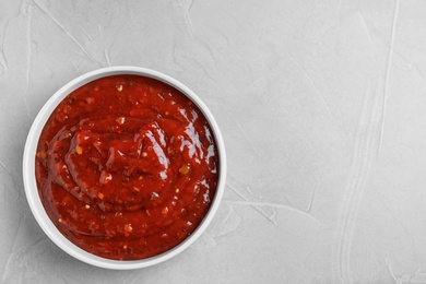 Bowl of hot chili sauce on light background, top view. Space for text