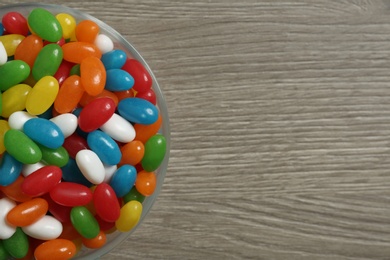 Photo of Top view of bowl with jelly beans on wooden background. Space for text