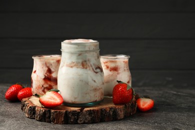 Photo of Tasty yoghurt with jam and strawberries on grey textured table, closeup. Space for text