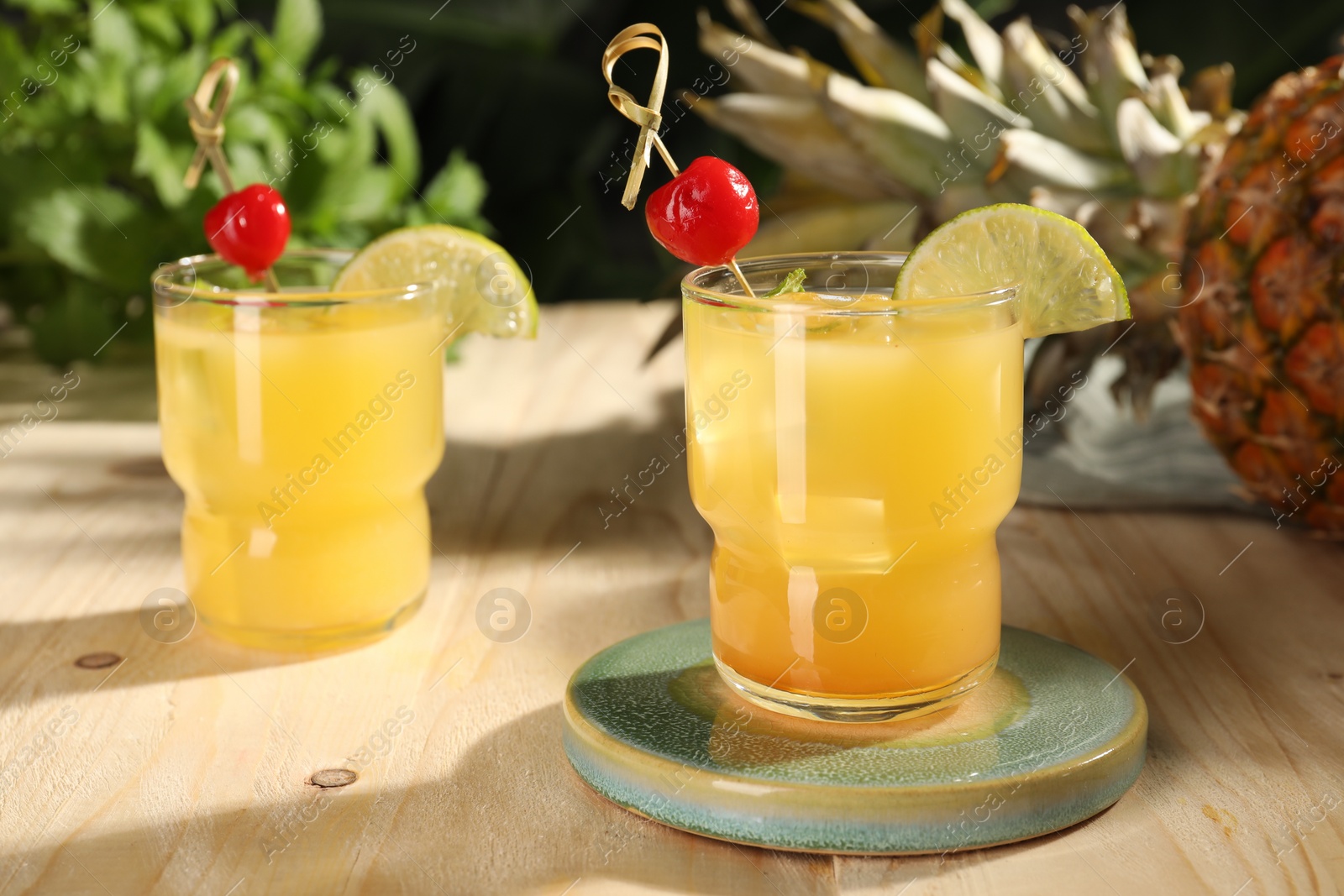 Photo of Tasty pineapple cocktails with cherry and lime on wooden table