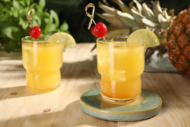 Photo of Tasty pineapple cocktails with cherry and lime on wooden table