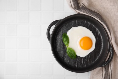 Tasty fried egg with basil in pan on white tiled table, flat lay. Space for text