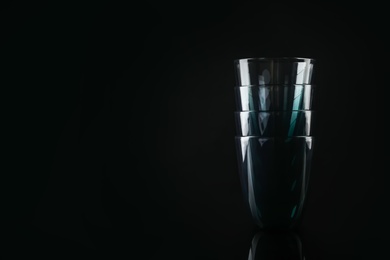 Photo of Stack of empty colorful glasses on black background, space for text