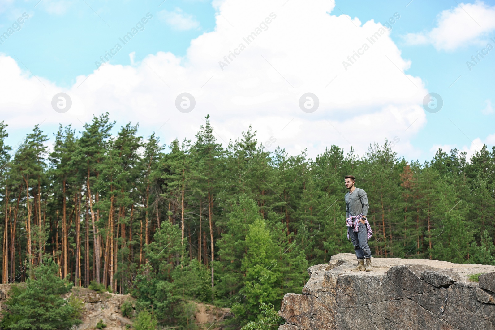 Photo of Young man on rock near beautiful forest. Camping season