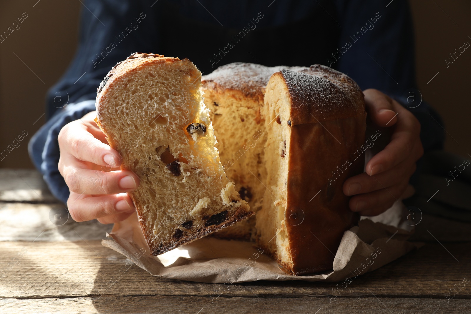 Photo of Woman taking slice of delicious Panettone cake with powdered sugar at wooden table, closeup. Traditional Italian pastry