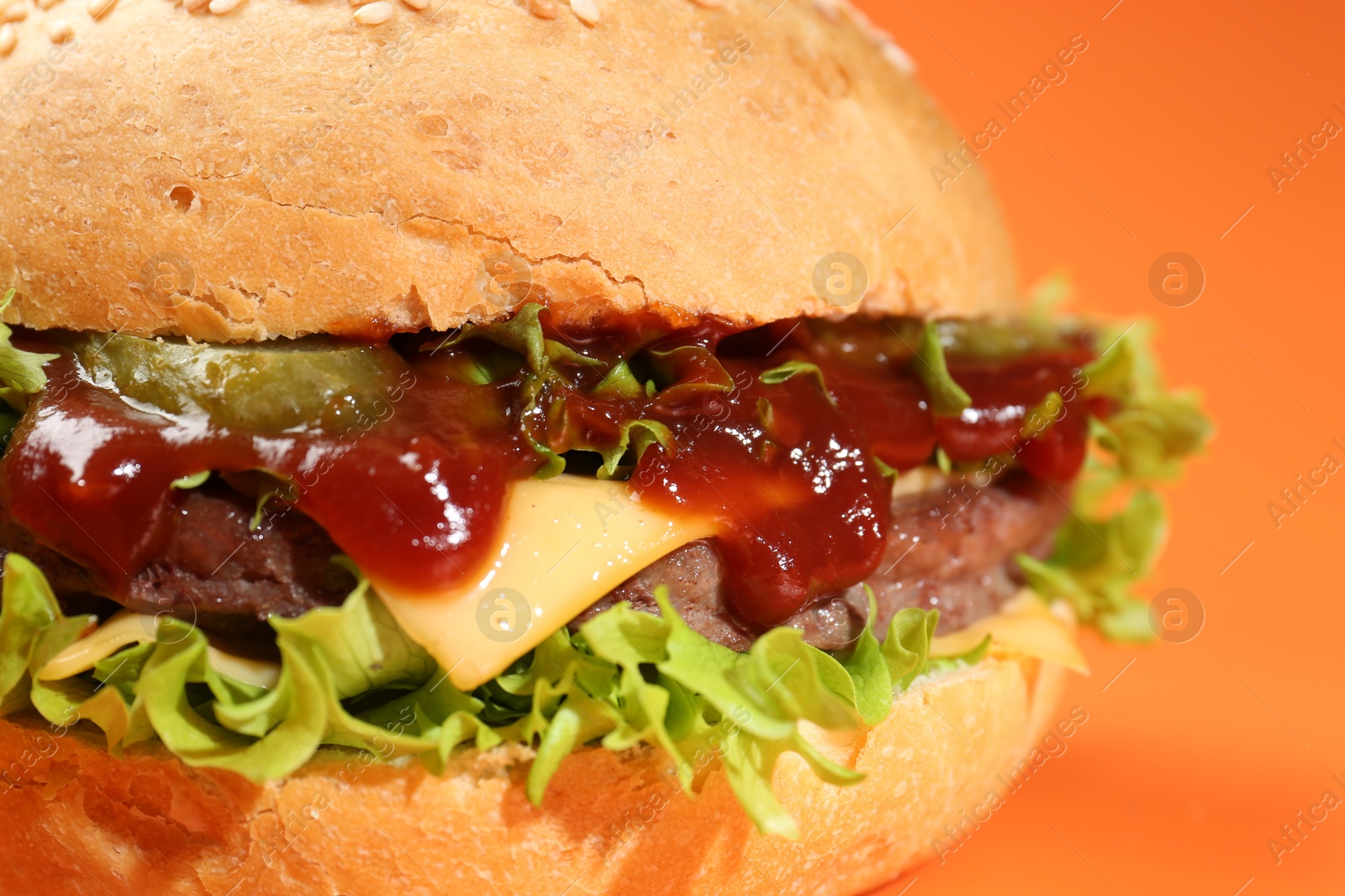 Photo of Delicious cheeseburger with lettuce, pickle, ketchup and patty on coral background, closeup