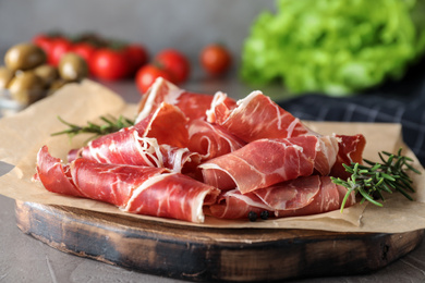 Photo of Slices of tasty prosciutto on grey table, closeup