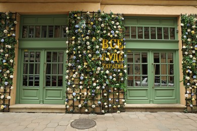 Photo of LVIV, UKRAINE - MAY, 27, 2022: Inscription Everything will be Ukraine written in ukrainian and arranged with flowers near entrance of building