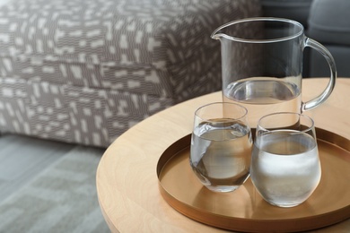 Tray with jug and glasses of water on wooden table in room, space for text. Refreshing drink