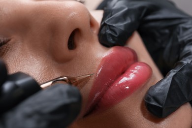 Young woman undergoing procedure of permanent lip makeup in tattoo salon, closeup