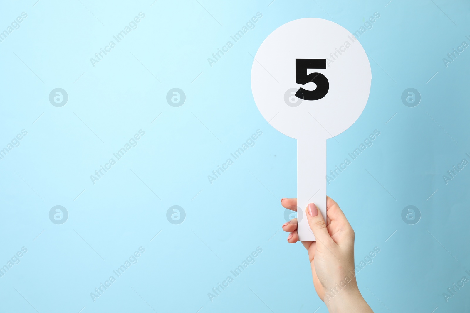 Photo of Woman holding auction paddle with number 5 on light blue background, closeup. Space for text