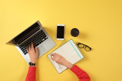 Woman working with modern laptop at color table, top view