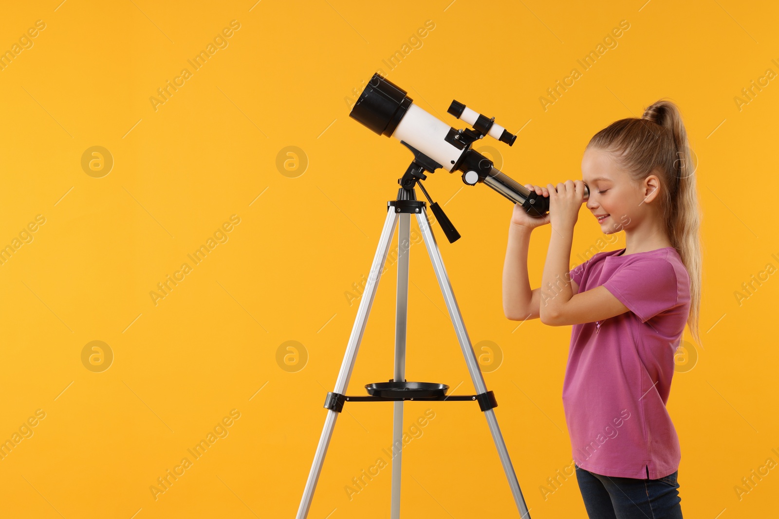 Photo of Happy little girl looking at stars through telescope on orange background, space for text