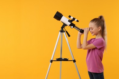 Photo of Happy little girl looking at stars through telescope on orange background, space for text