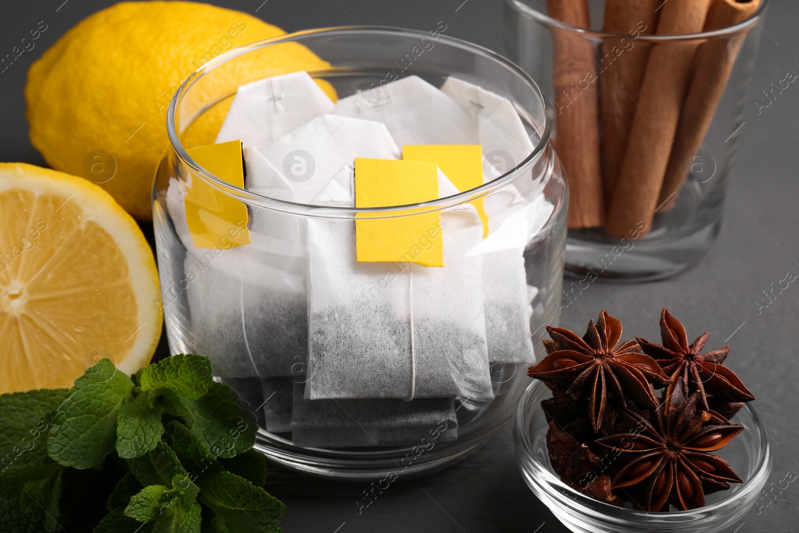 Photo of Tea bags, anise stars, cinnamon sticks, mint and lemon on grey wooden table, closeup