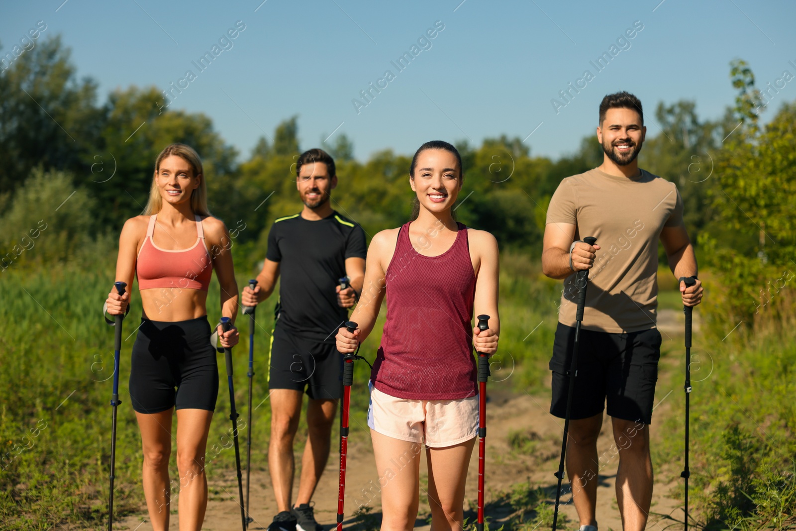 Photo of Group of happy people practicing Nordic walking with poles outdoors on sunny day