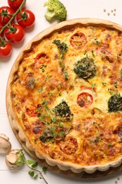 Delicious homemade quiche and different vegetables on white table, flat lay