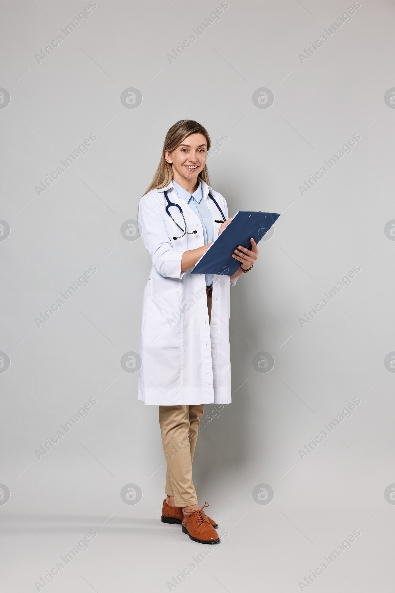 Photo of Portrait of happy doctor with stethoscope and clipboard on light grey background