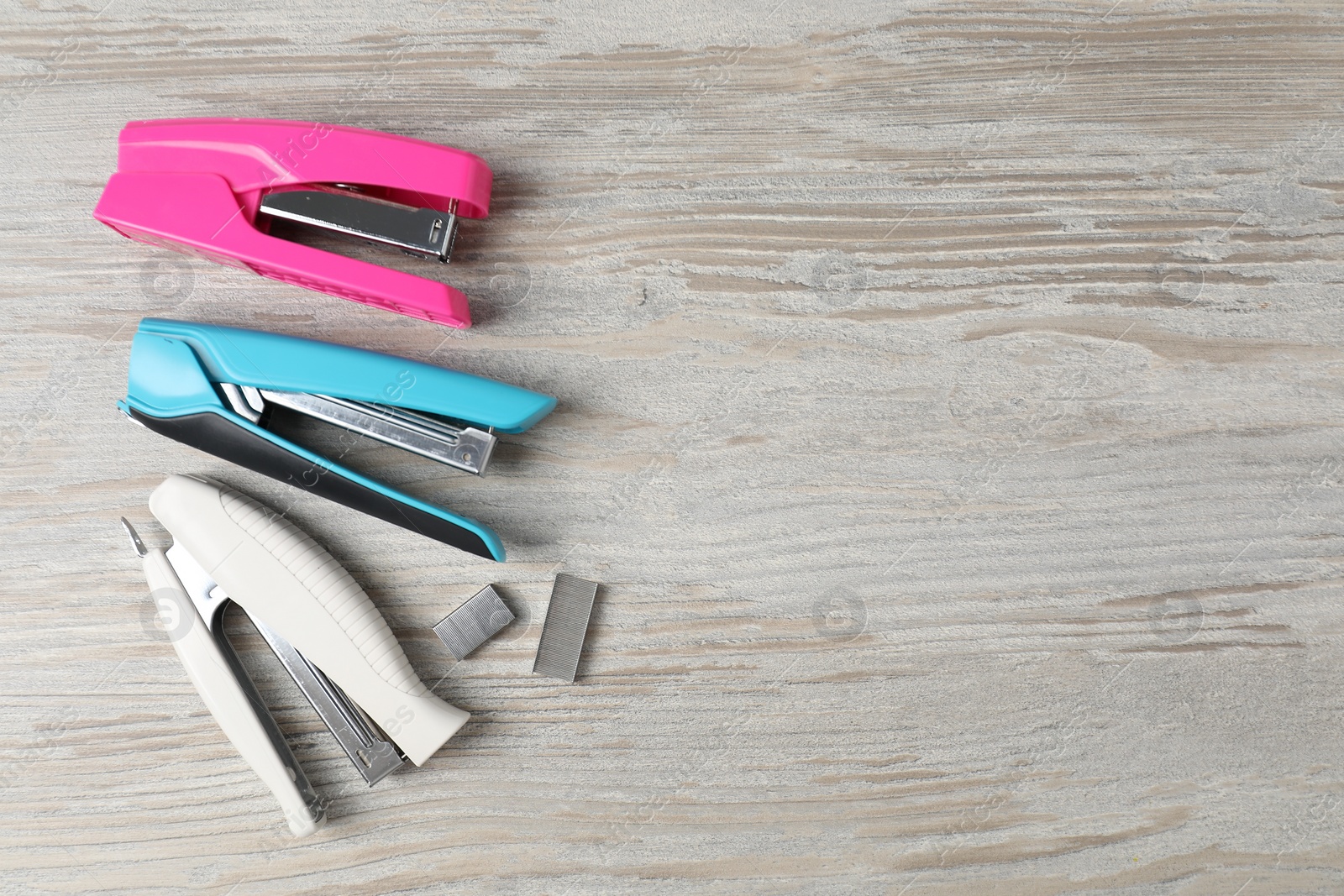 Photo of Color staplers and metal staples on wooden table, flat lay. Space for text