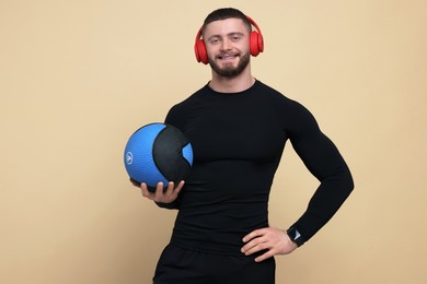 Photo of Handsome sportsman with headphones and medicine ball on brown background, space for text