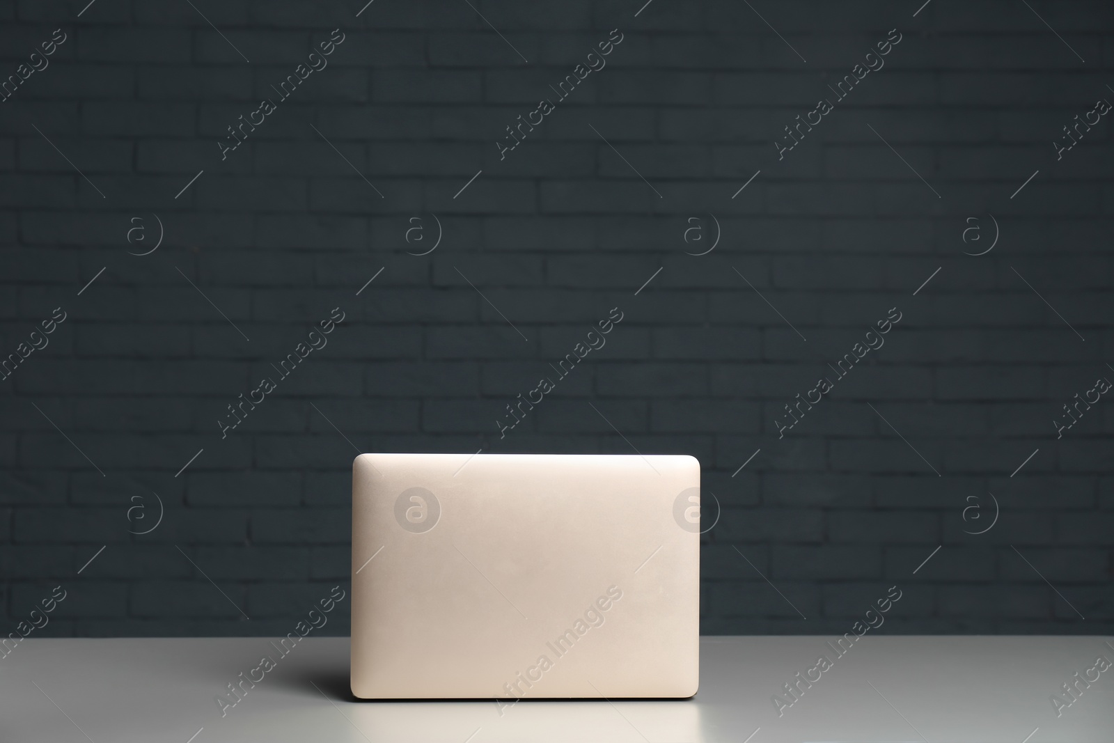 Photo of Modern laptop on table against brick wall
