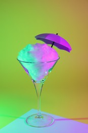 Beautiful martini glass with cotton candy and umbrella on color background