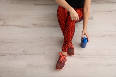 Photo of Woman in sportswear with bottle of water sitting on floor indoors, top view. Space for text