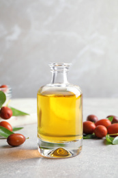 Jojoba oil in glass bottle and seeds on light grey table