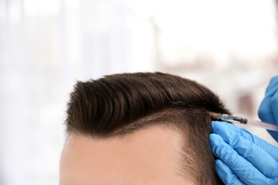 Photo of Young man with hair loss problem receiving injection on blurred background, closeup