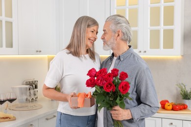 Photo of Happy affectionate senior couple with gift box and beautiful bouquet indoors