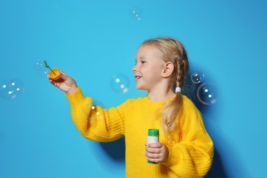 Photo of Cute little girl blowing soap bubbles on color background