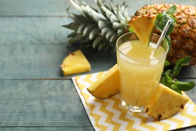 Photo of Delicious pineapple juice and fresh fruit on blue wooden table. Space for text