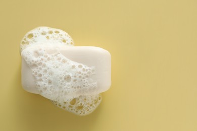 Photo of Soap bar with fluffy foam on yellow background, top view. Space for text