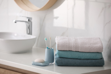 Photo of Stack of fresh towels, toothbrushes and soap bar on countertop in bathroom