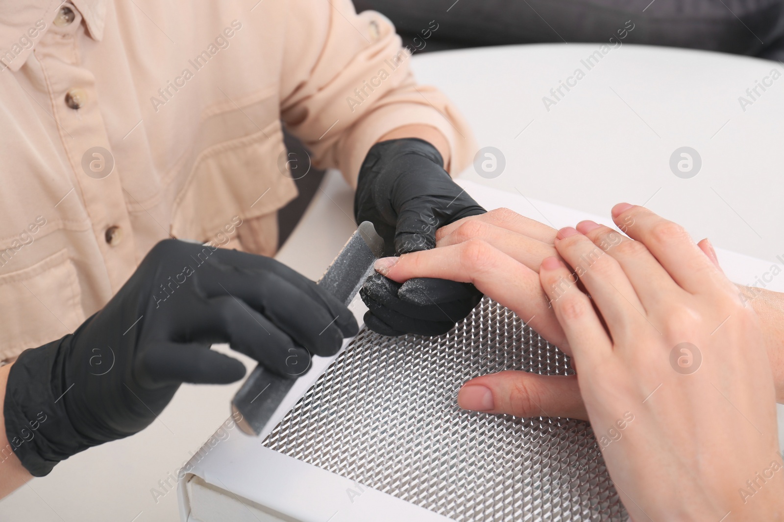 Photo of Professional manicurist working with client at white table, closeup