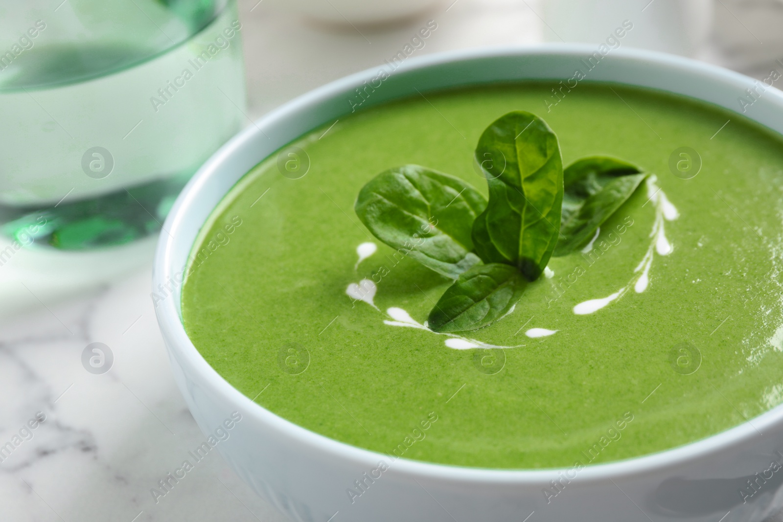 Photo of Bowl of healthy green soup with fresh spinach on marble table, closeup view