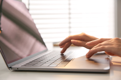 Photo of Woman working with modern laptop at white table, closeup