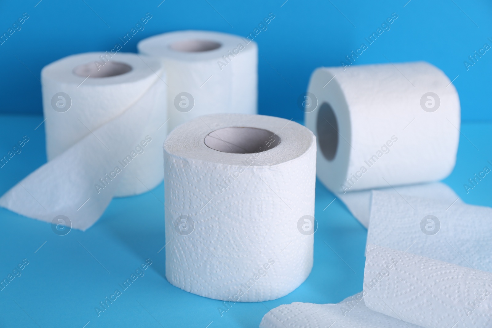 Photo of Soft toilet paper rolls on light blue background, closeup