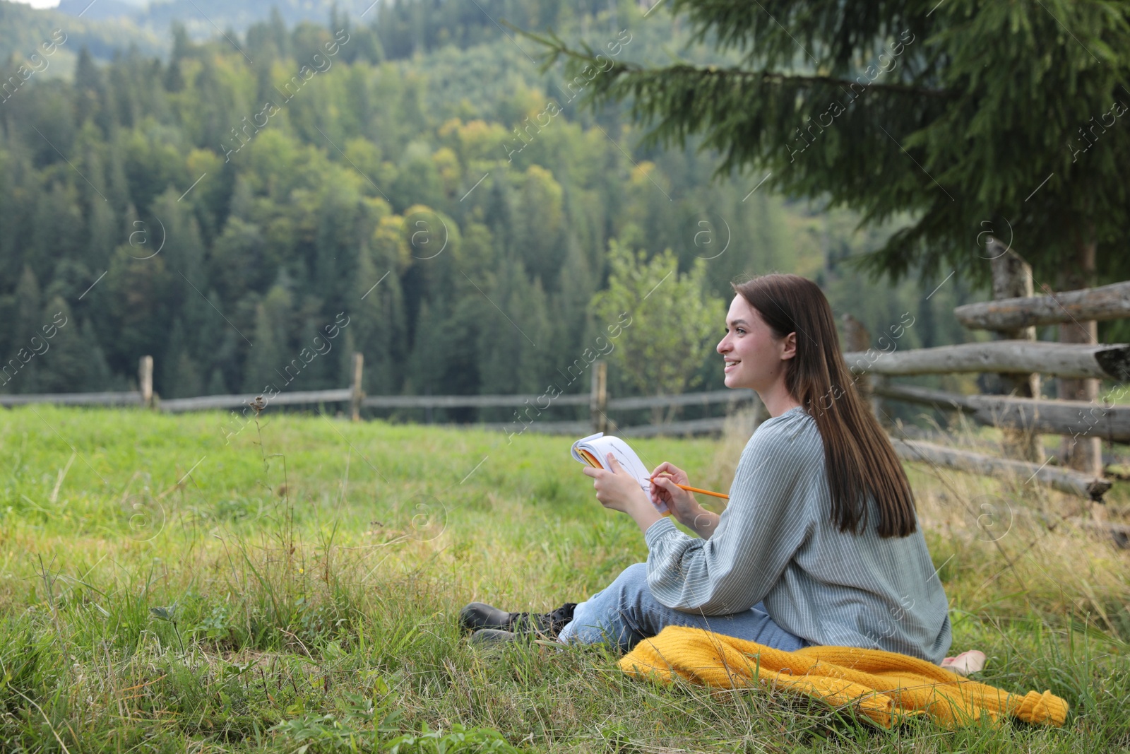 Photo of Beautiful young woman drawing with pencil in notepad on green grass