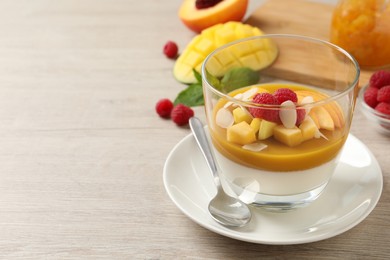 Photo of Delicious panna cotta with mango coulis, fresh fruit pieces and almond flakes on light wooden table. Space for text