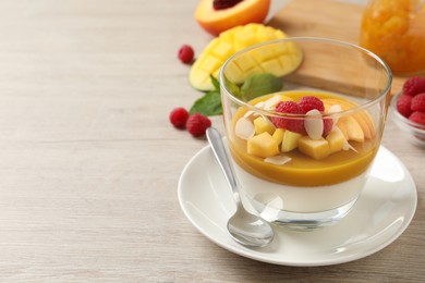 Delicious panna cotta with mango coulis, fresh fruit pieces and almond flakes on light wooden table. Space for text