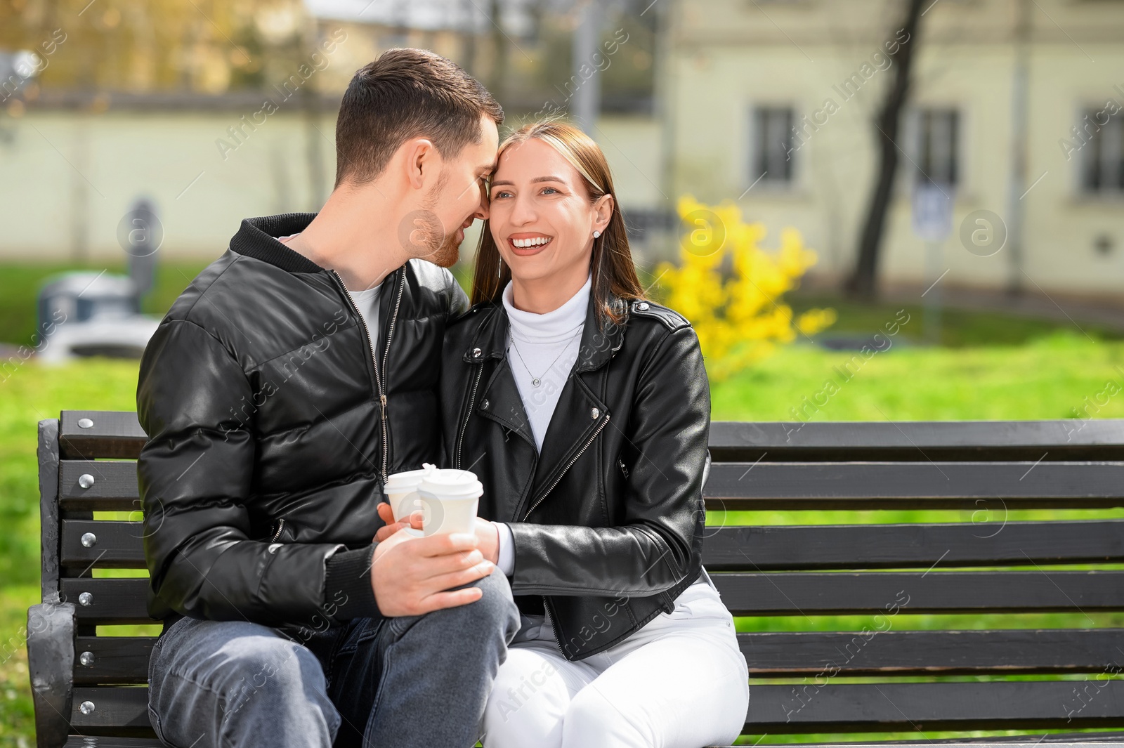 Photo of Lovely young couple with cups of coffee on bench outdoors. Romantic date