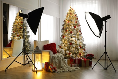 Cozy festive photo zone with armchair, Christmas tree and professional equipment indoors