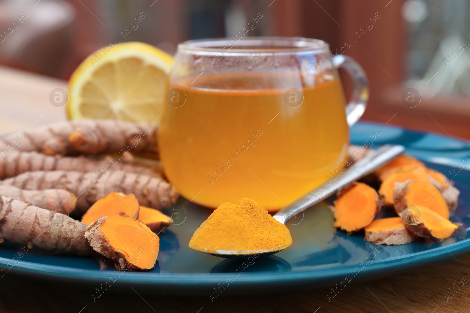 Photo of Plate with glass cup of hot tea, lemon, turmeric powder and roots on table